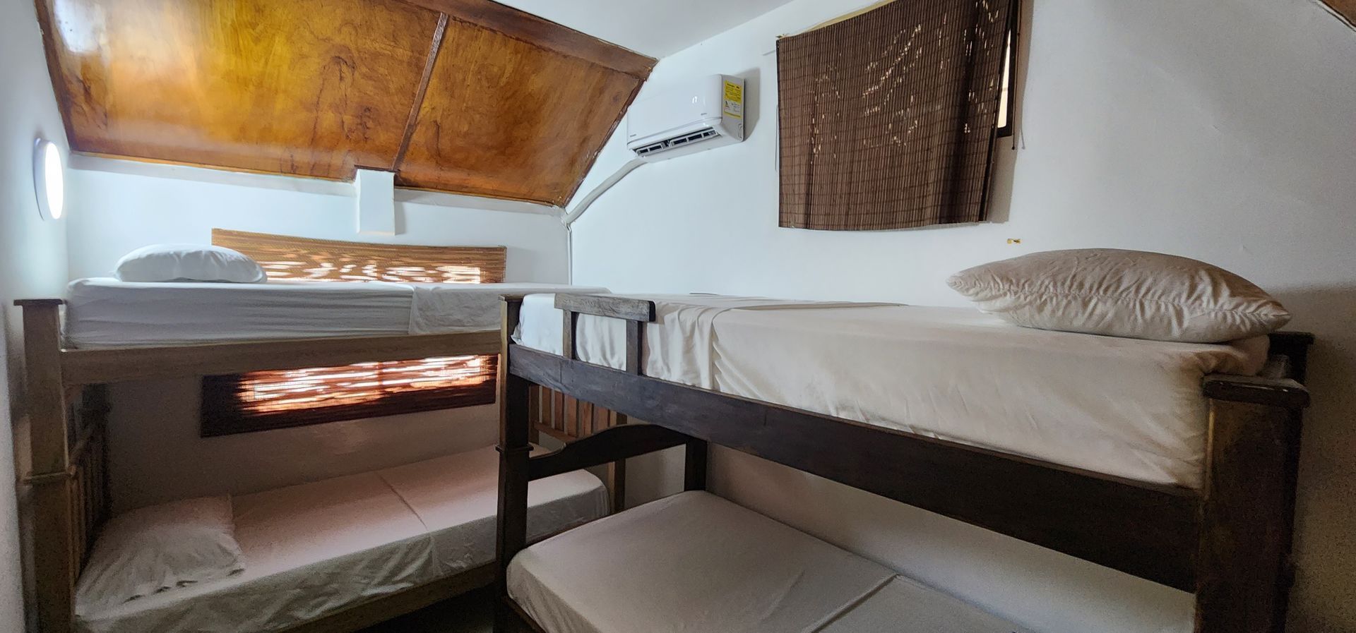 Una acogedora habitación con dos literas de madera bajo un techo inclinado revestido de paneles de madera, con ropa de cama sencilla y paredes blancas.