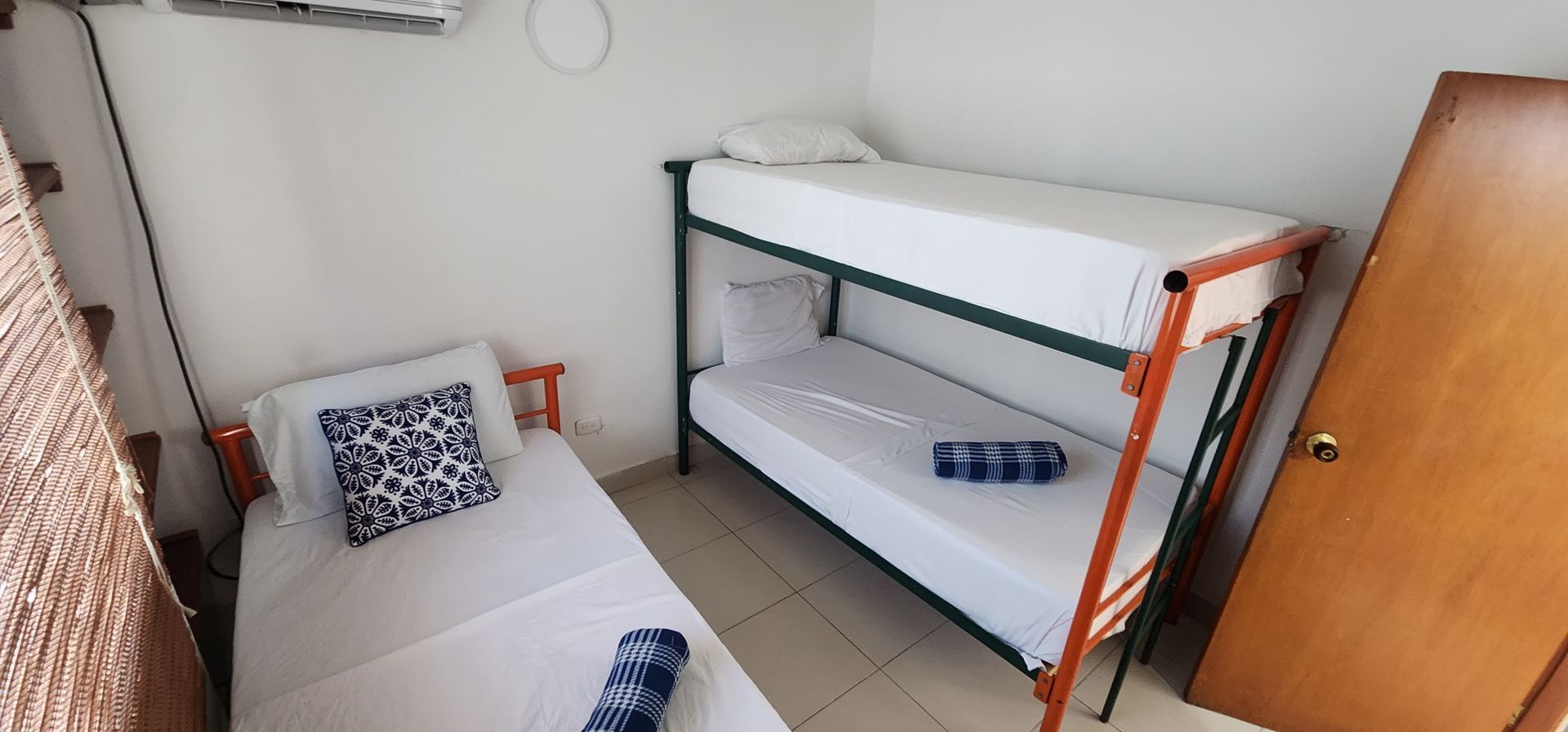Una pequeña habitación de hotel con una cama individual de madera y una litera de metal, ambas con sábanas blancas y toallas azules enrolladas.