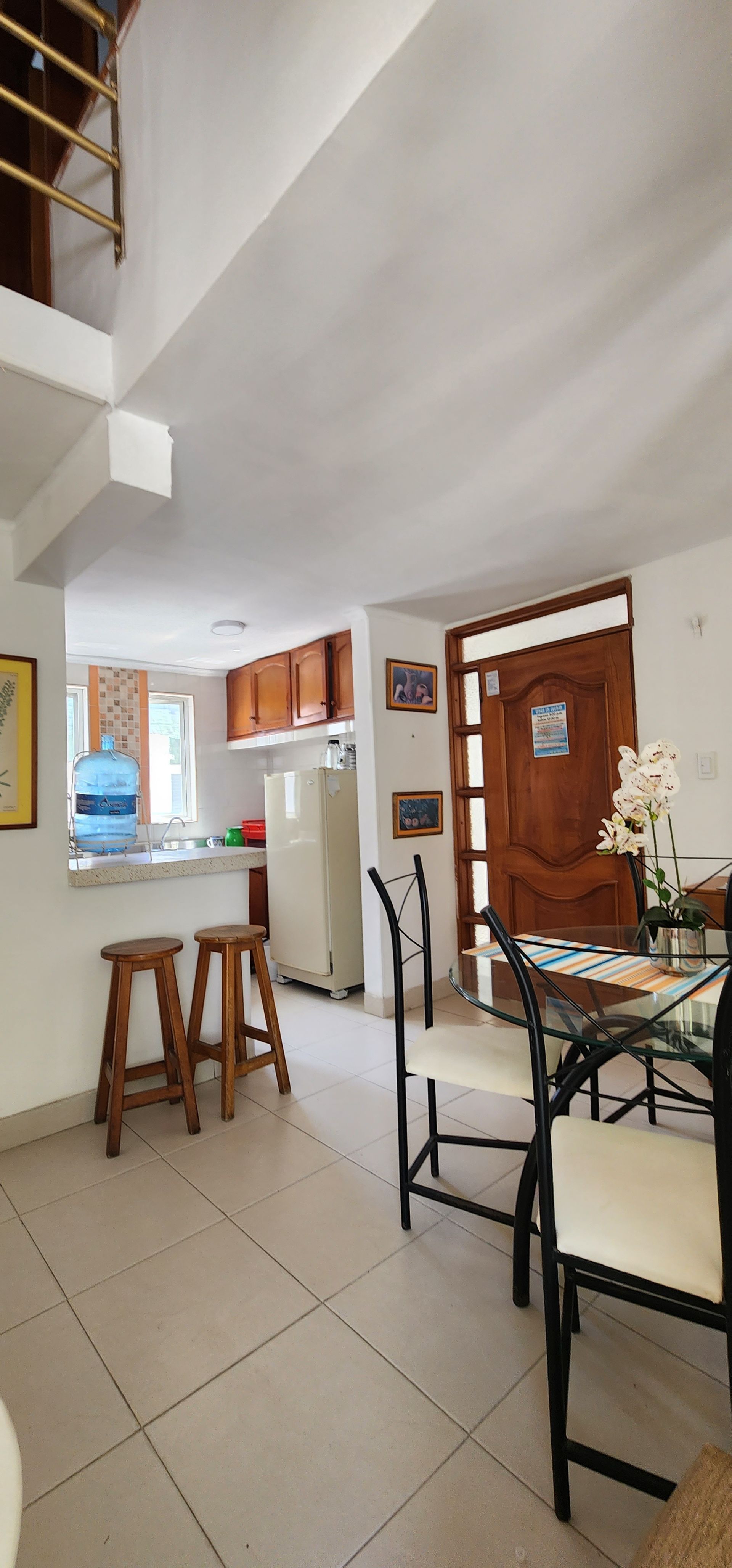 Una habitación diáfana con una barra de desayuno con dos taburetes de madera, una zona de cocina con armarios y una mesa de comedor.