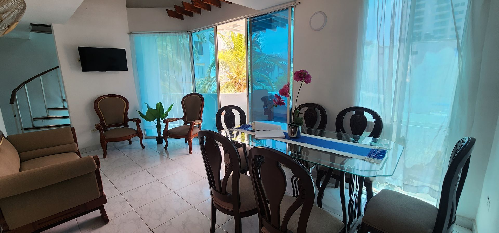 El luminoso comedor cuenta con una mesa de cristal con seis sillas, una pequeña zona de estar con dos sillones y un sofá.