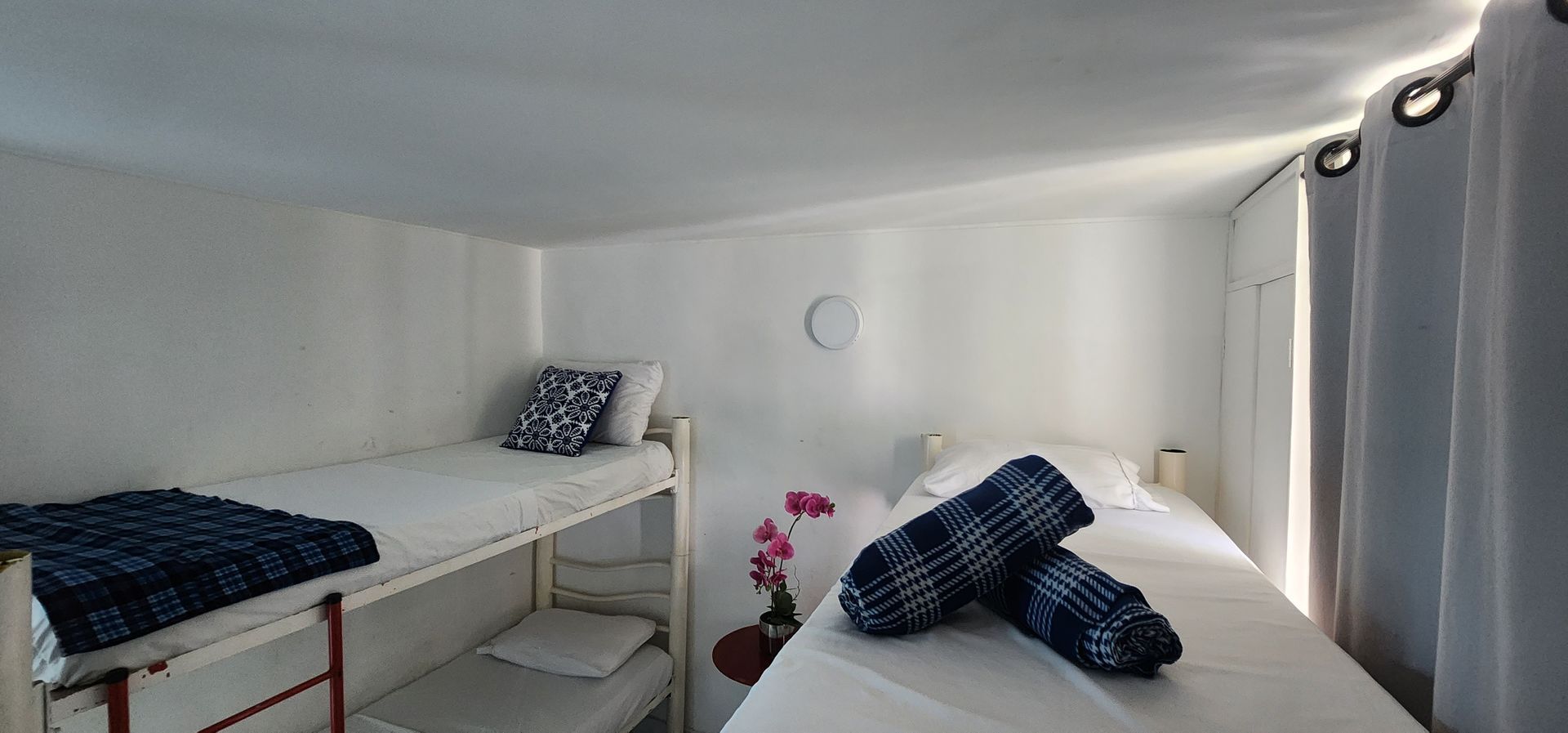 Un dormitorio blanco con una litera a la izquierda, una cama individual a la derecha y cortinas en el extremo derecho.