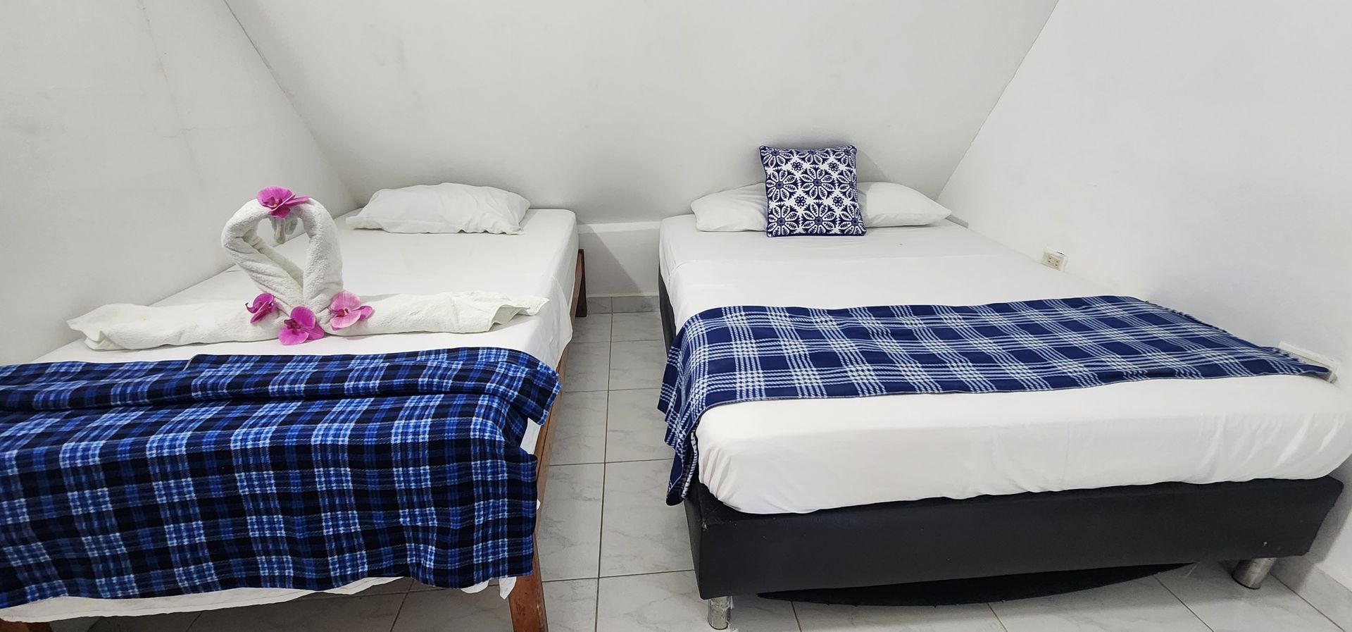 Una habitación de hotel con dos camas, cada una cubierta con una manta de cuadros azules, situada bajo un techo blanco inclinado.