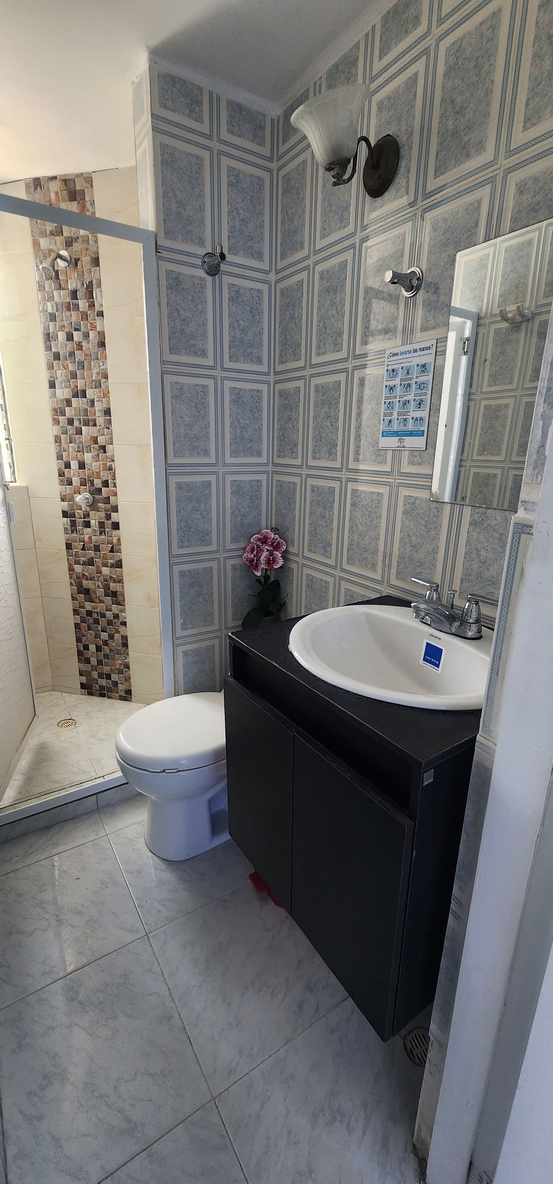 Un baño con papel pintado gris estampado, un lavabo blanco con pedestal, un inodoro y una cabina de ducha alicatada.