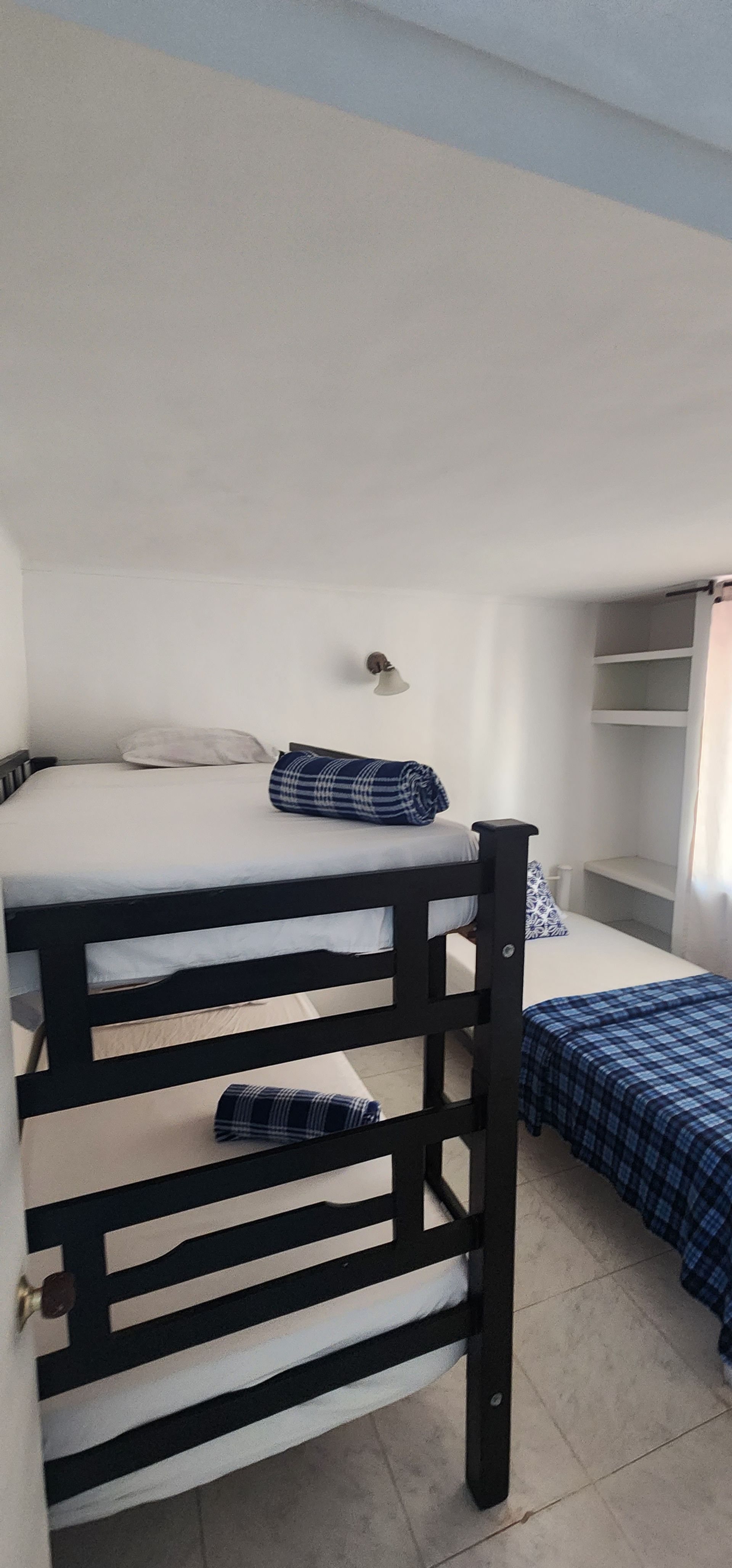 Un dormitorio con una litera de madera negra con ropa de cama estampada en azul y una cama individual con sábanas a juego cerca.
