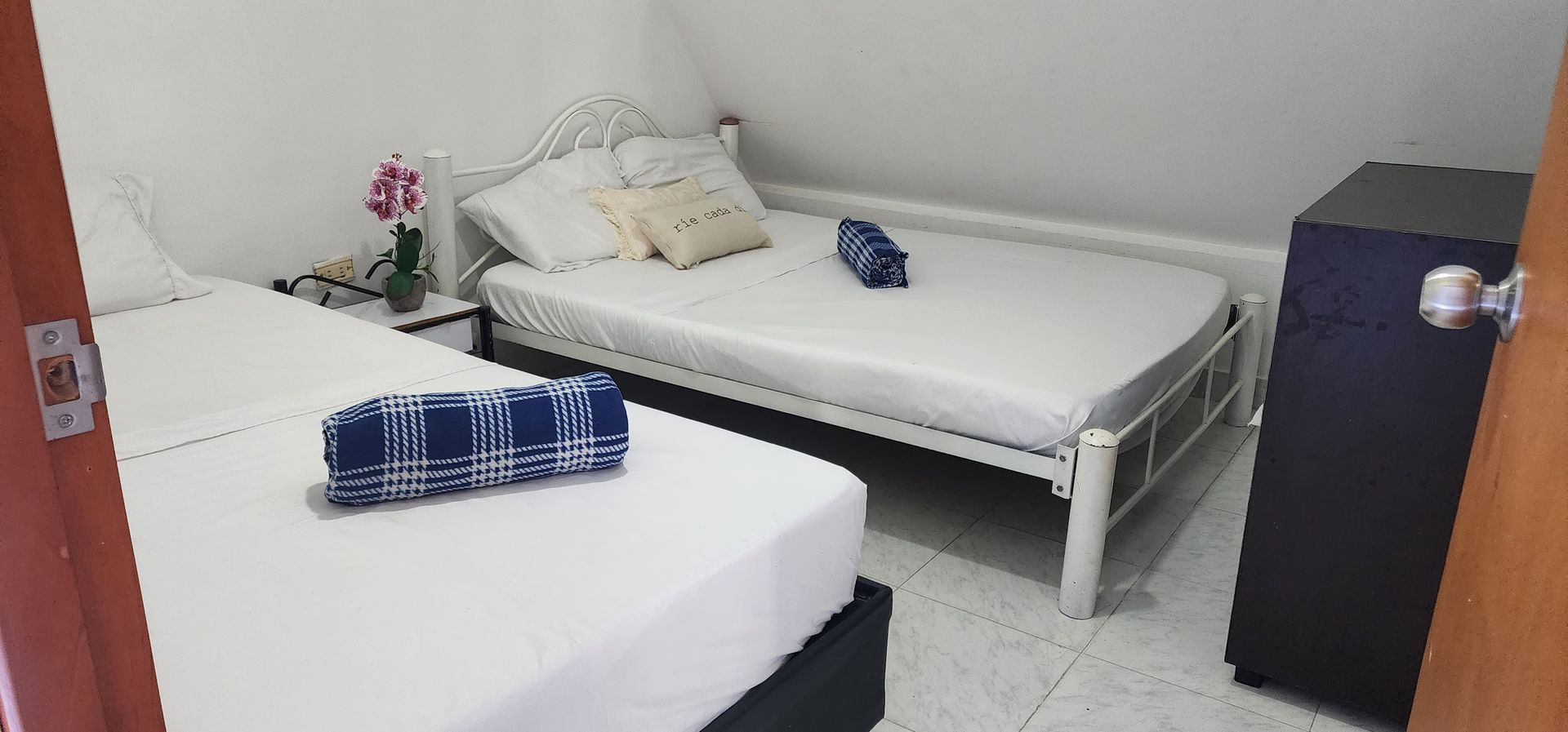 Un dormitorio con dos camas con sábanas blancas, cada una cubierta con una toalla doblada de estampado azul y blanco.