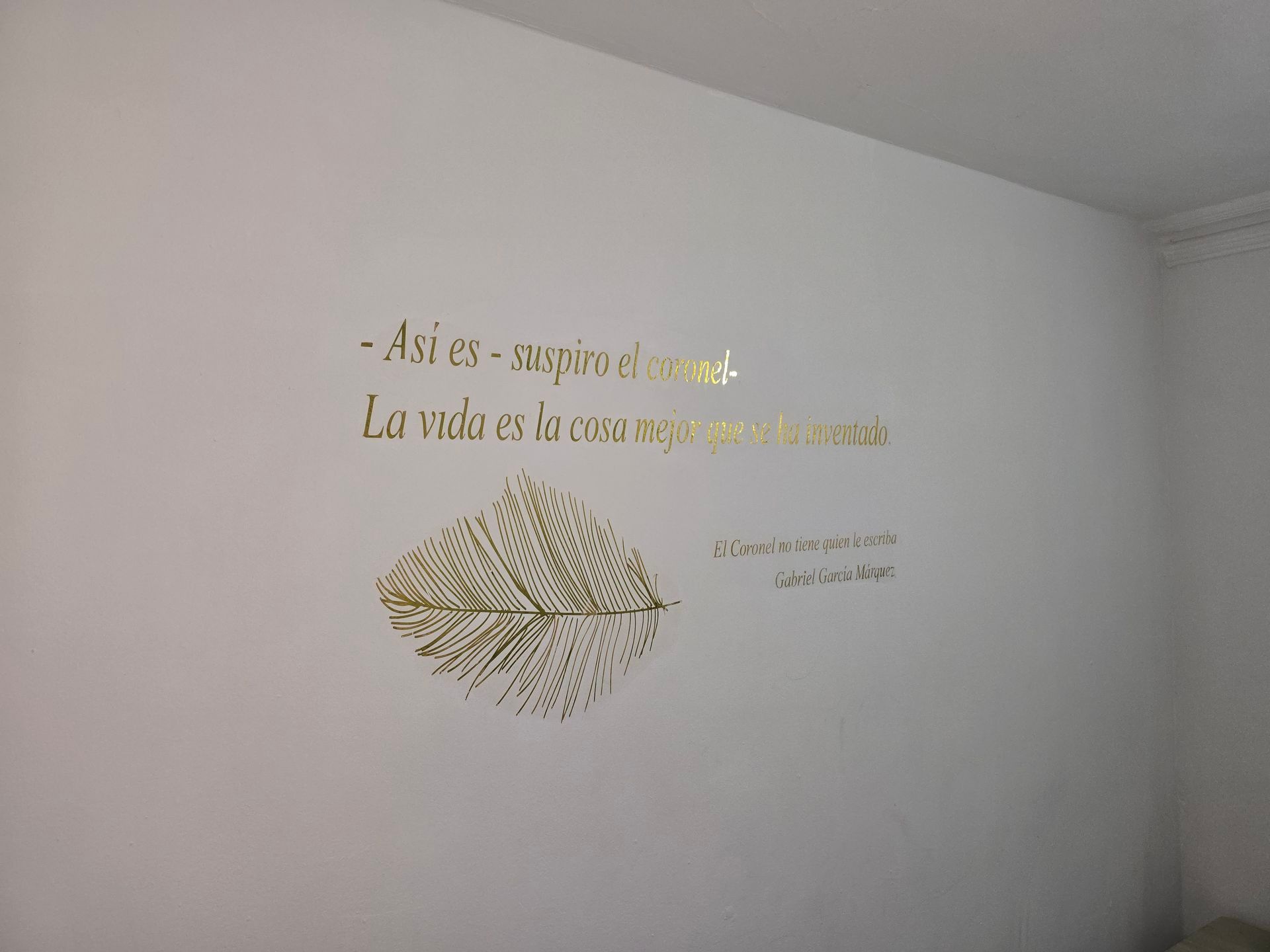 Una pared blanca decorada con texto en letra cursiva dorada 