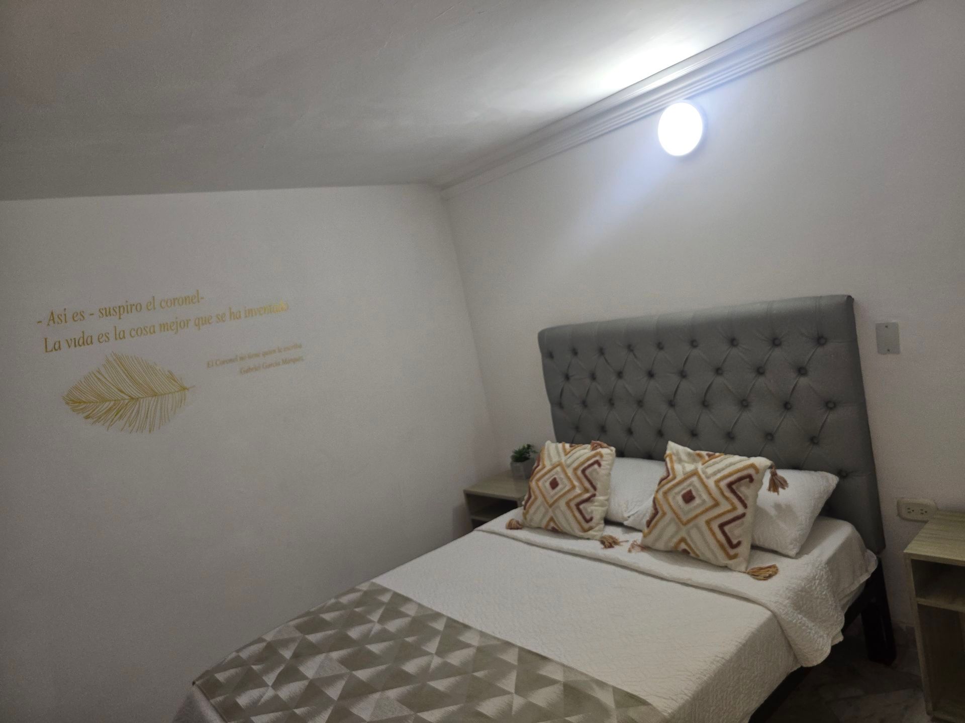 Un dormitorio con cabecero acolchado gris, ropa de cama blanca 