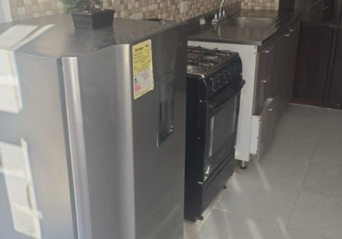 En una habitación con suelo de baldosas, un frigorífico gris se encuentra junto a una estufa negra y una encimera de cocina.