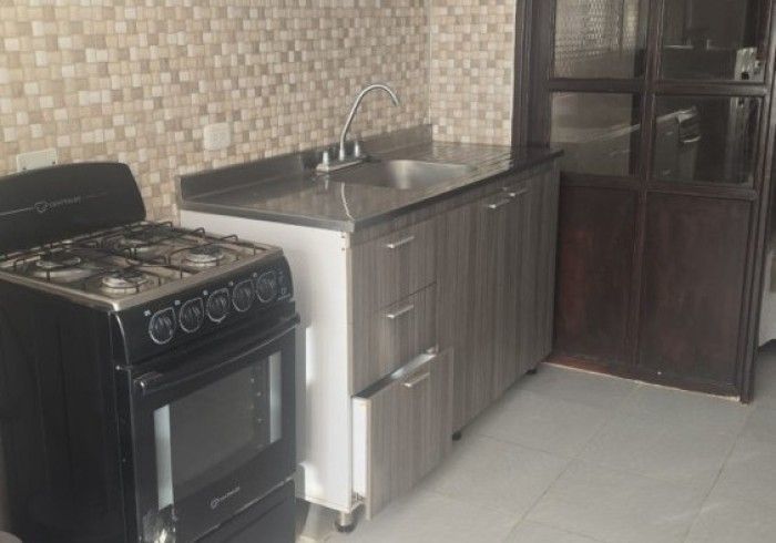 Una estufa de gas negra se encuentra junto a un mueble de cocina de madera gris con encimera y fregadero de acero inoxidable.