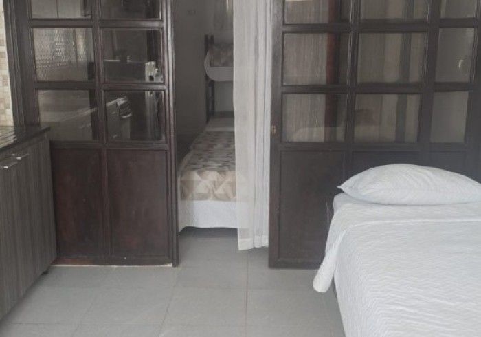 El interior de un dormitorio con una cama individual en primer plano y una vista, a través de puertas de cristal con marco de madera, de una segunda cama.