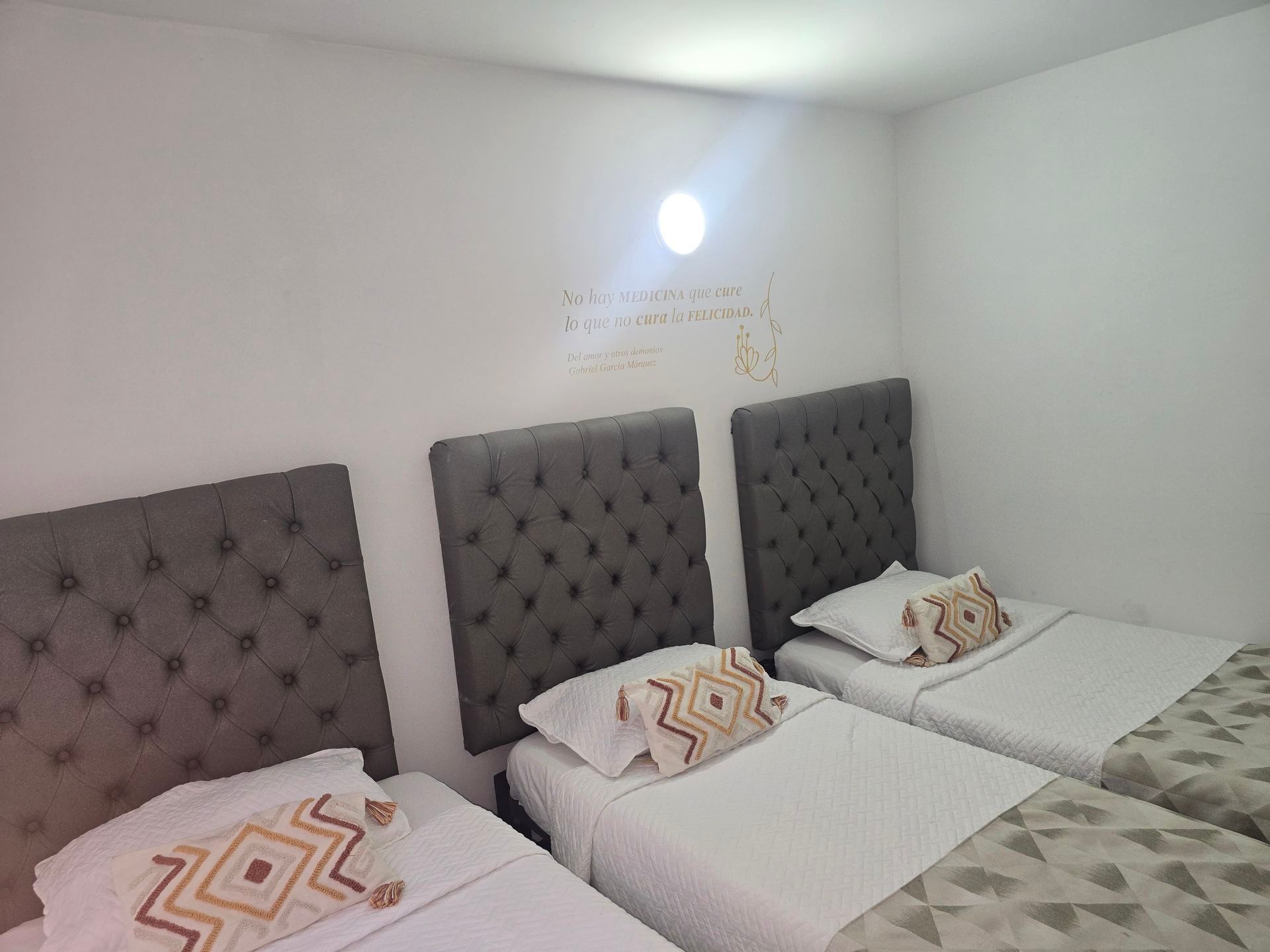Un dormitorio con tres camas individuales con cabeceros acolchados de color gris