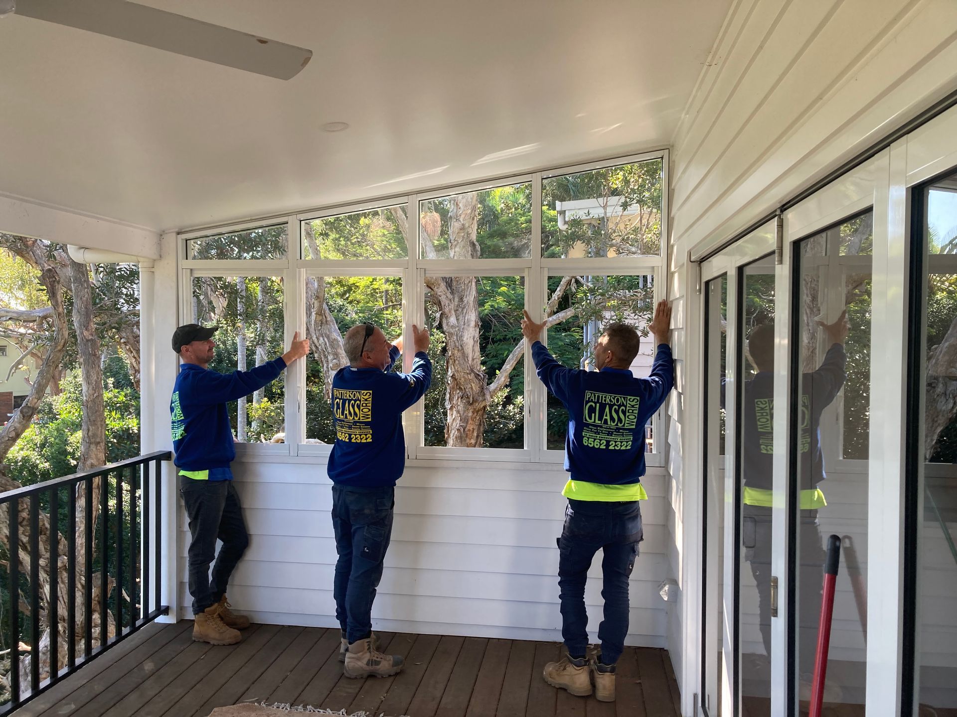 Three men are working on a window on a porch. — Patterson Glass Works in Kempsey, NSW