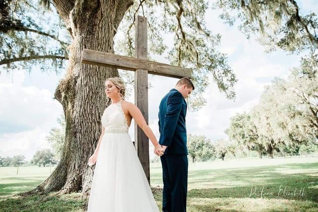 A bride and groom are holding hands in front of a wooden cross.
