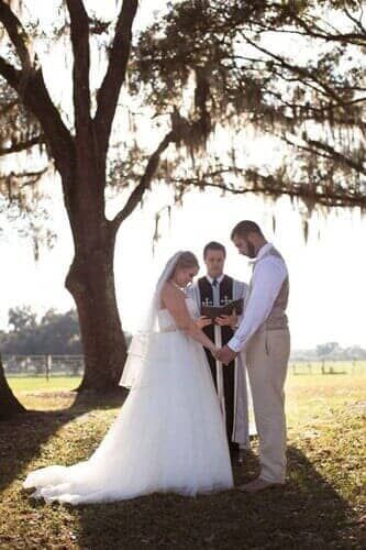 A bride and groom are holding hands during their wedding ceremony under a tree.