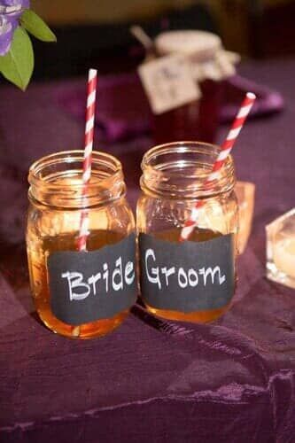 Two mason jars with straws labeled bride and groom are on a table.