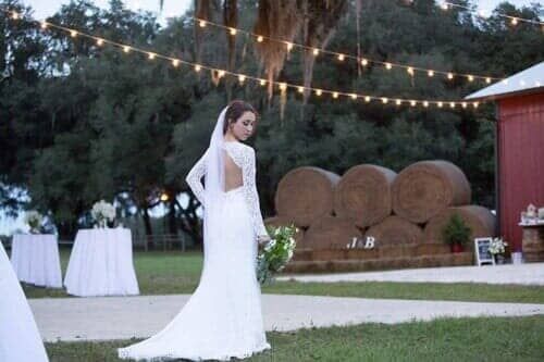 A bride in a wedding dress is standing in front of hay bales.