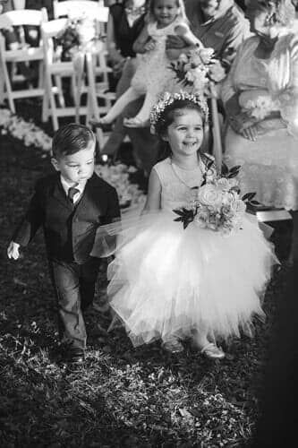 A black and white photo of a flower girl and ring bearer walking down the aisle at a wedding.