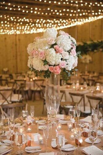 A large vase filled with pink and white flowers is on a table at a wedding reception.