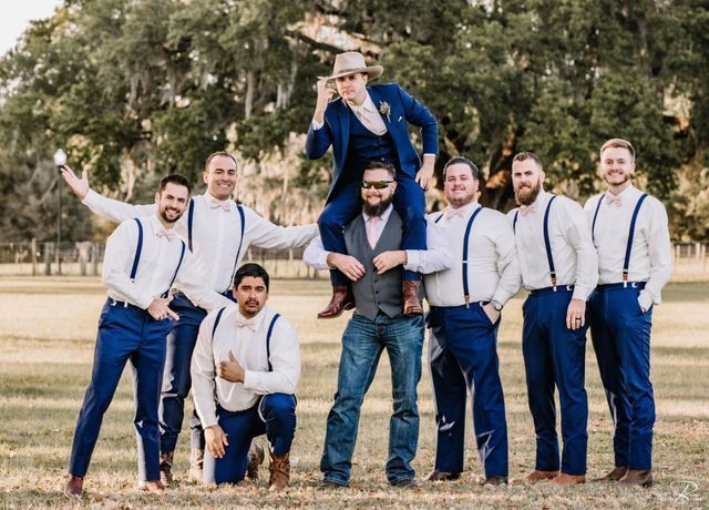 The groom and his groomsmen are posing for a picture in a field.