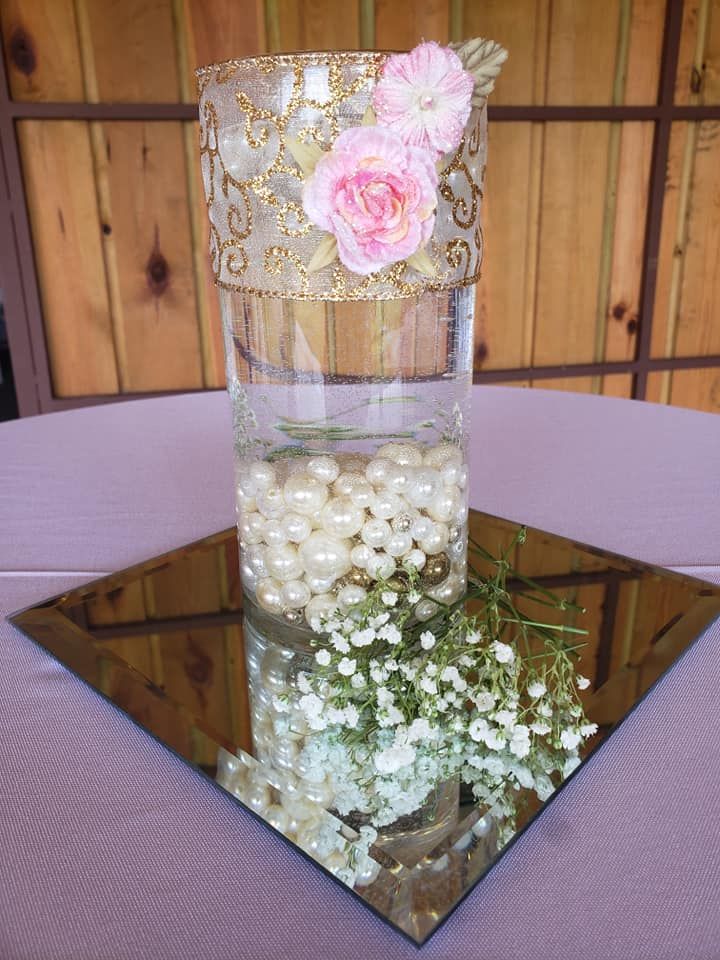 A vase filled with pearls and flowers is sitting on a mirror on a table.