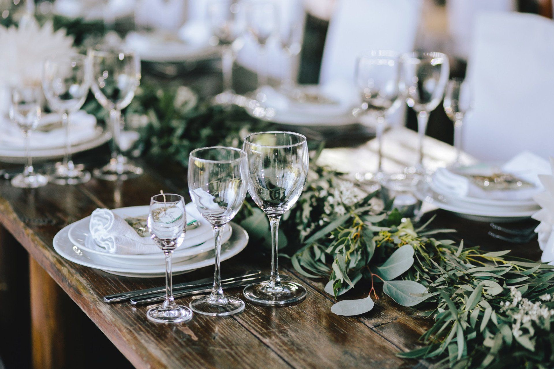 A wooden table with plates , wine glasses , and a garland of leaves.