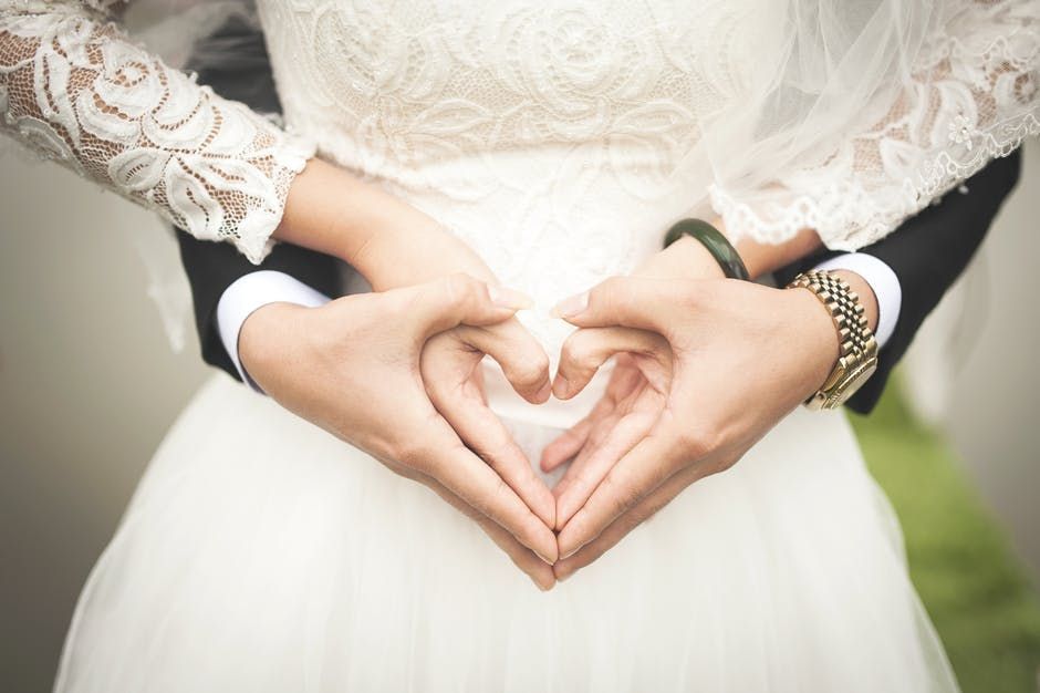 A bride and groom are making a heart shape with their hands.