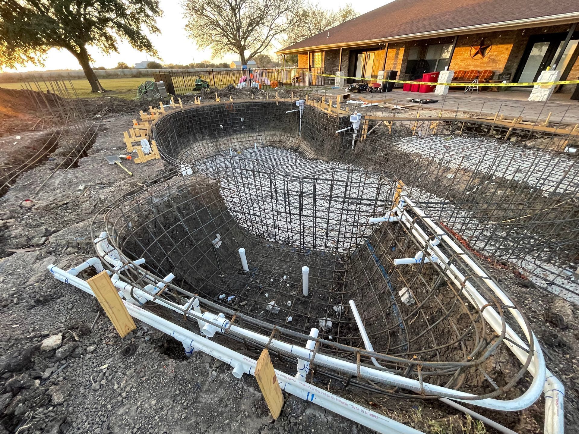 Pool under construction; rebar cage, plumbing, and gravel base visible.