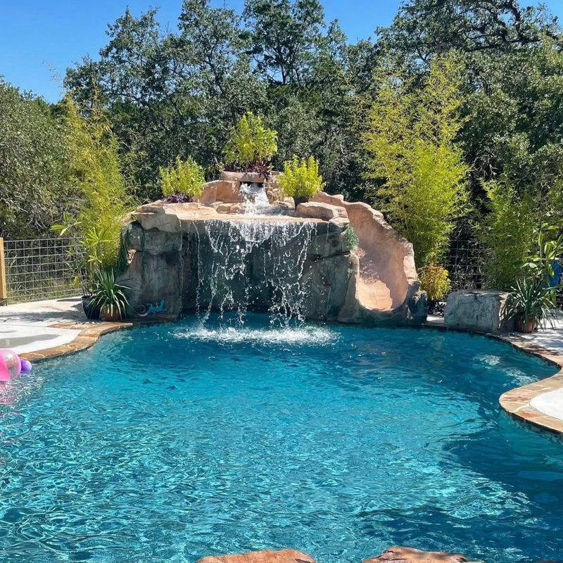 Swimming pool with a rock waterfall feature surrounded by lush greenery.