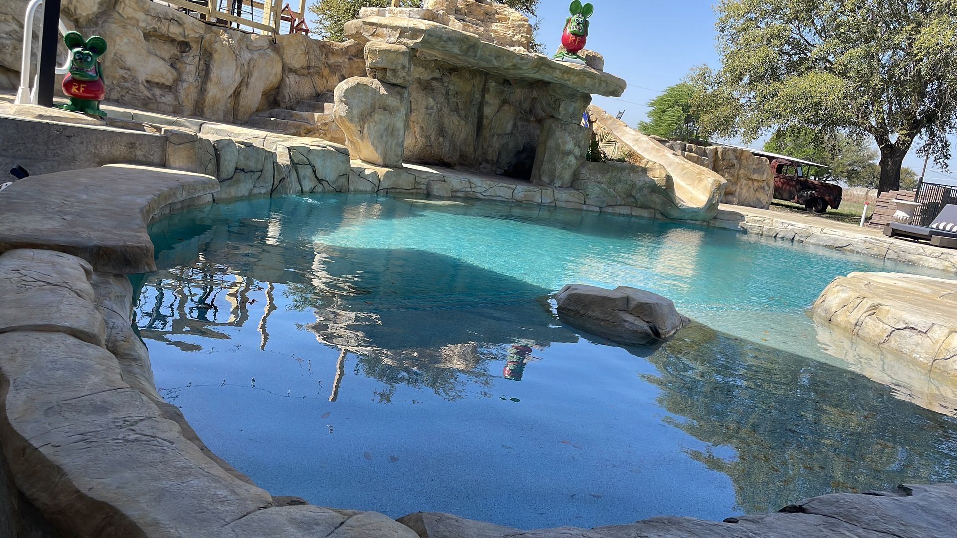 A pool with a waterfall feature surrounded by rock formations, under a bright sky.