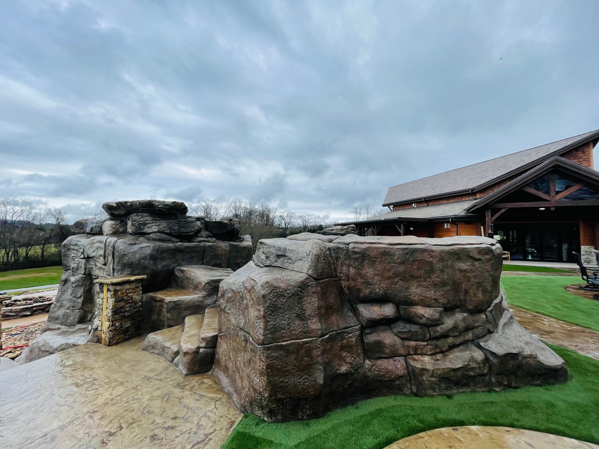 Artificial rock formations with steps near a wooden building under a cloudy sky.