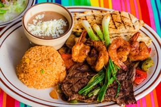 A plate of food with shrimp , steak , rice and beans on a colorful table cloth.