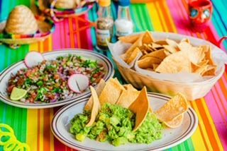 A colorful table topped with plates of guacamole and tortilla chips.
