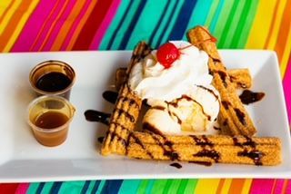 A plate of churros with ice cream , whipped cream and a cherry on top.