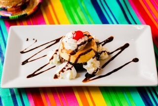 A white plate topped with a dessert with whipped cream and a cherry on top.