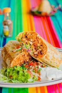 A burrito is cut in half on a plate on a colorful table cloth.