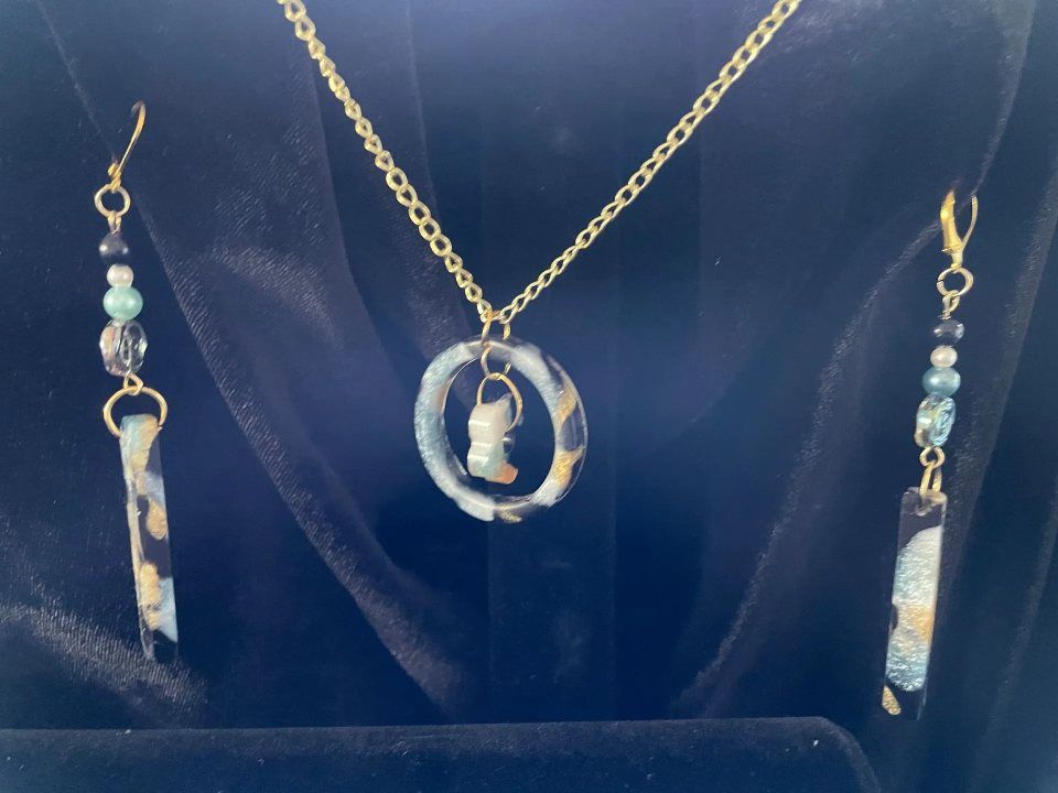 Gold necklace and earrings set with a pendant of a profile and blue and gold accents, displayed on black velvet.