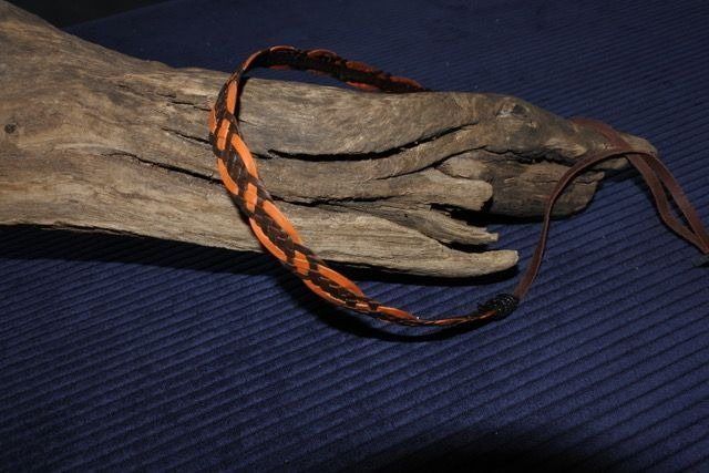 Braided orange and brown strap on a weathered wooden surface, likely for a camera.