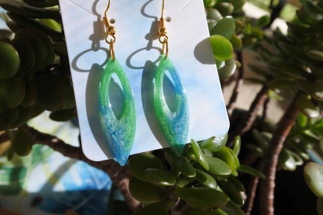 Blue and green oval-shaped resin earrings with gold hooks on a white card, with a jade plant background.