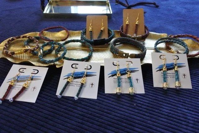 Jewelry display: braided leather bracelets and earrings on gold trays against a blue surface.