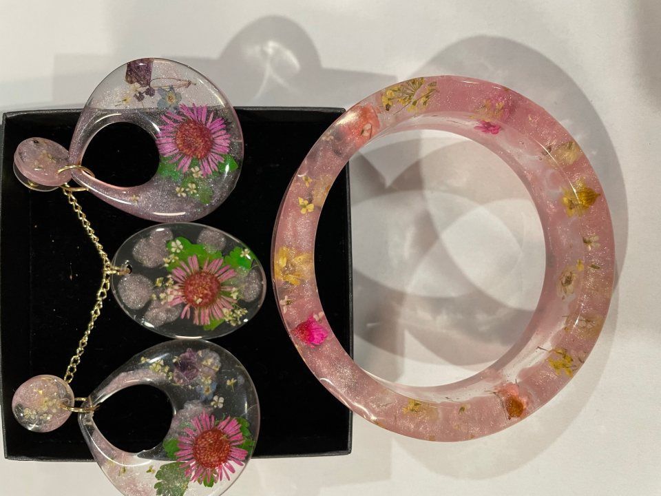 Resin jewelry set: pink, flower-filled pendant earrings and bracelet on a black box, white surface.