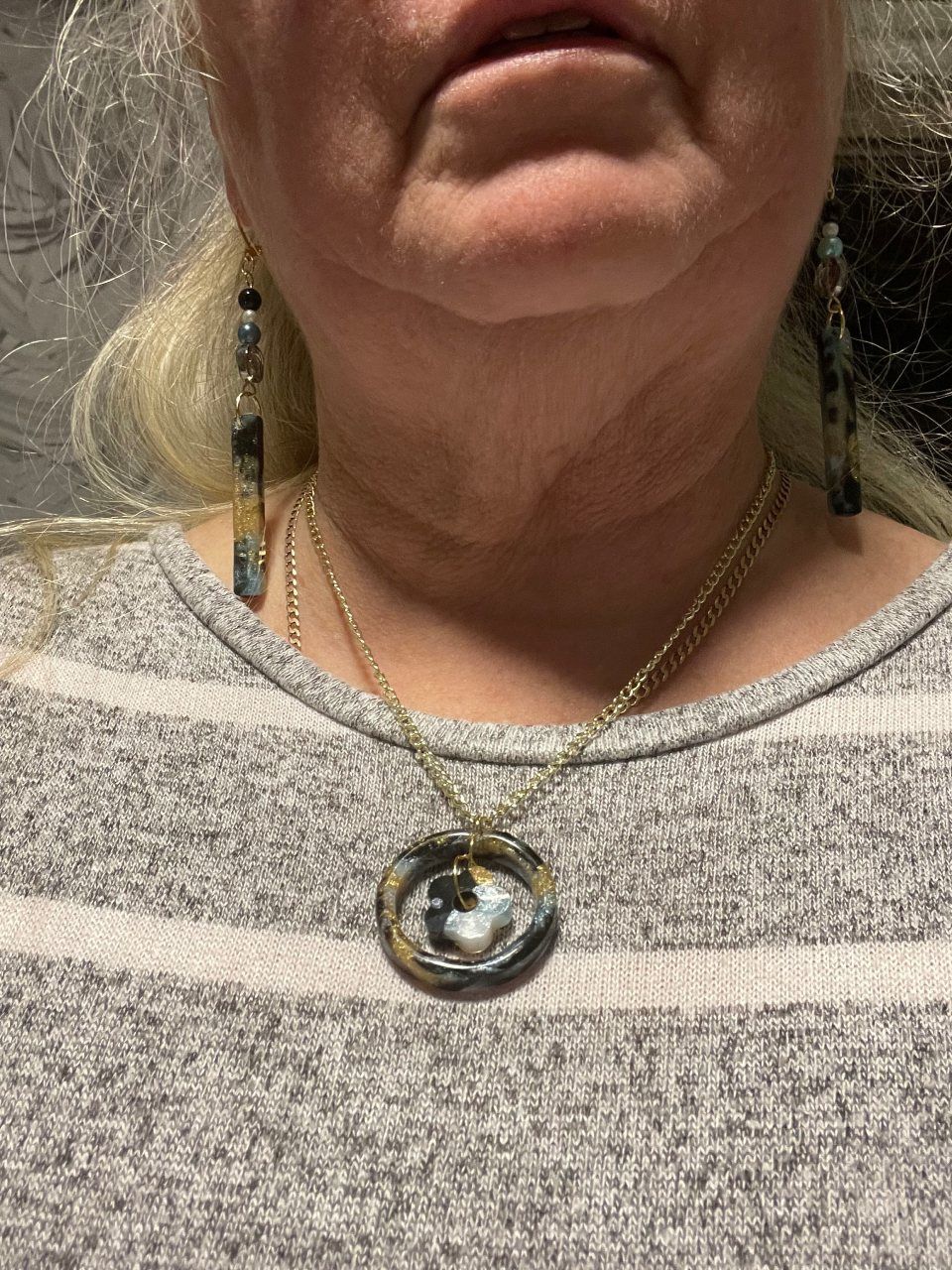Person wearing a gold necklace with pendant and matching dangling earrings; gray striped shirt.