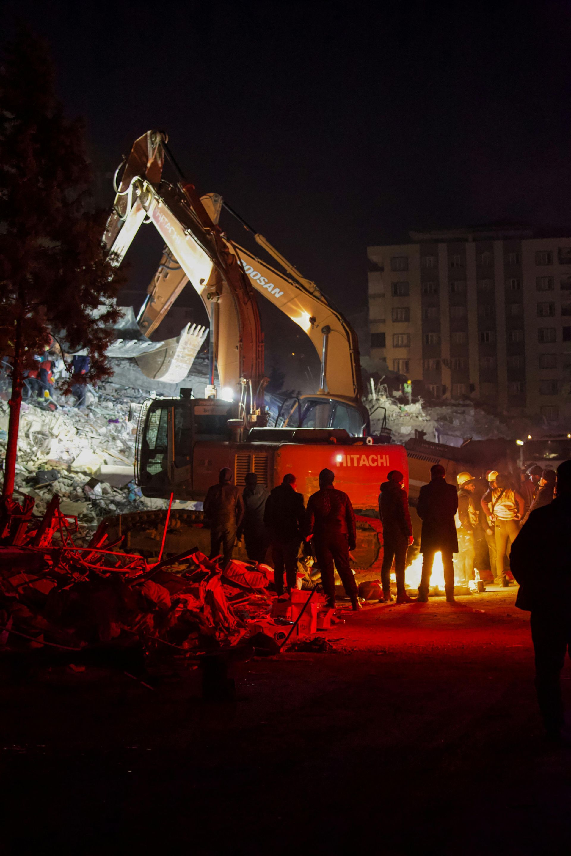 A group of people are standing around a construction site at night.