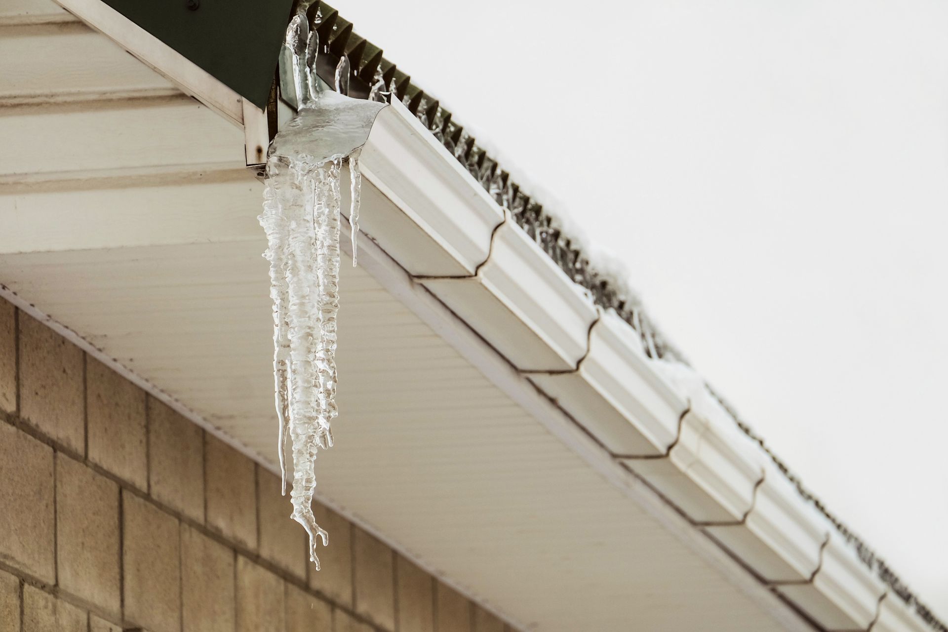 Icicles hanging from a white gutter on a building with brick siding.