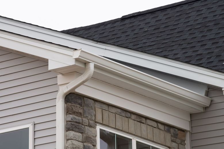White gutters attached to a house with gray siding, stone facade, and a dark roof.