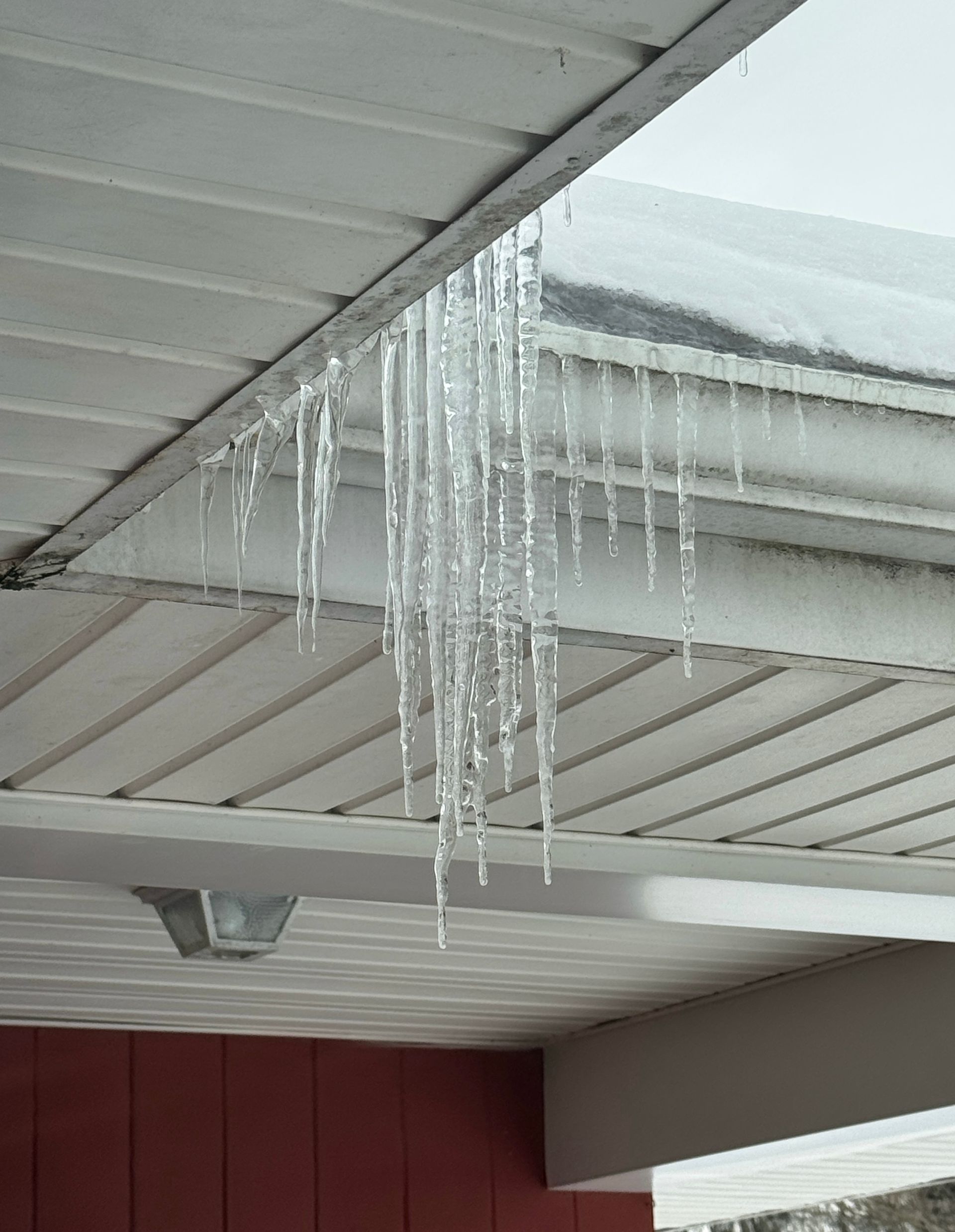Icicles hanging from a white roof overhang. Red building visible below.