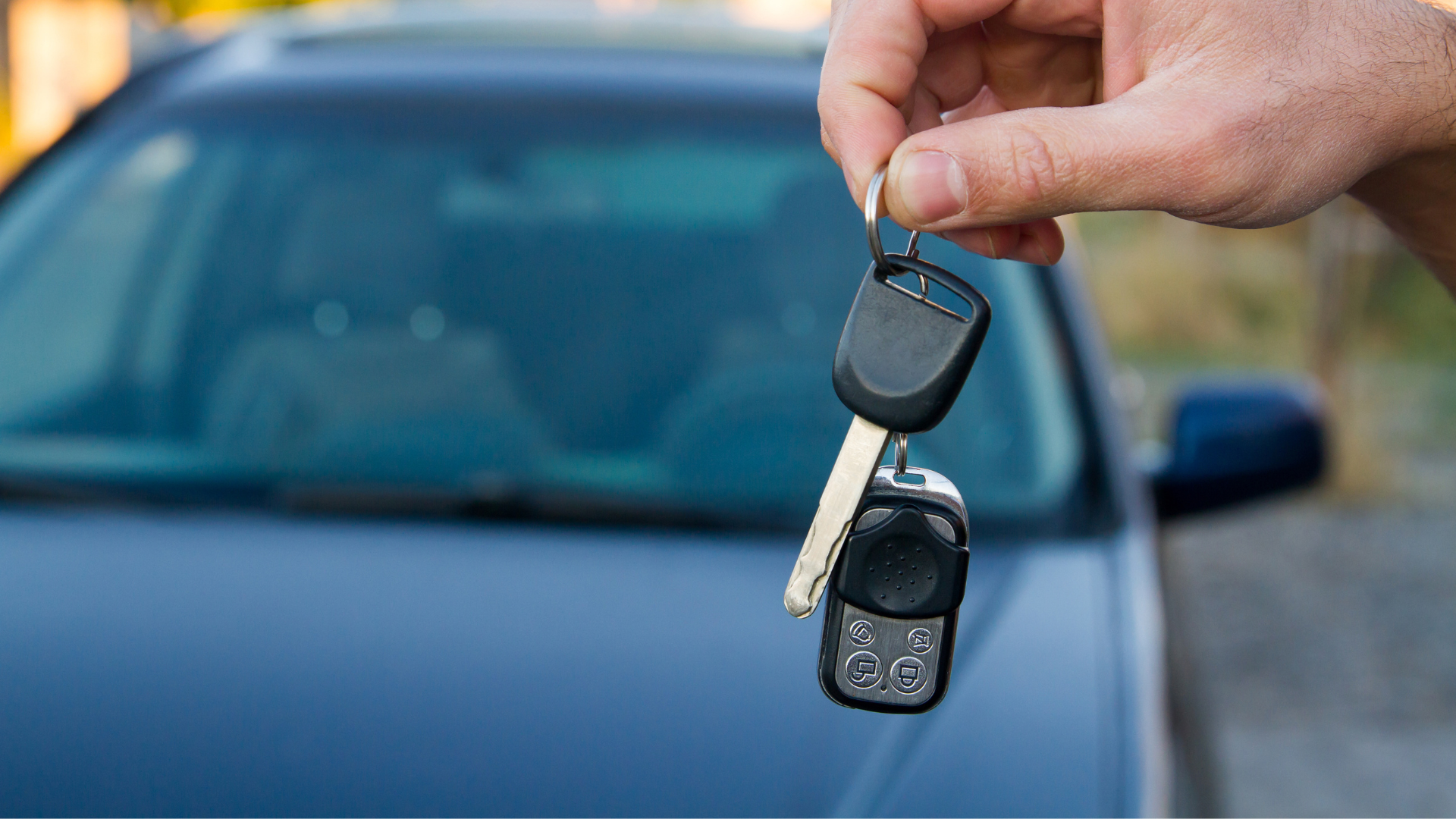 A person is holding a car key in front of a car.