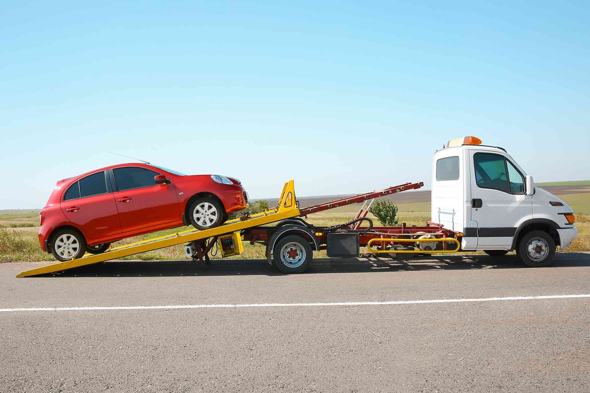 A red car is being towed by a tow truck on the side of the road.