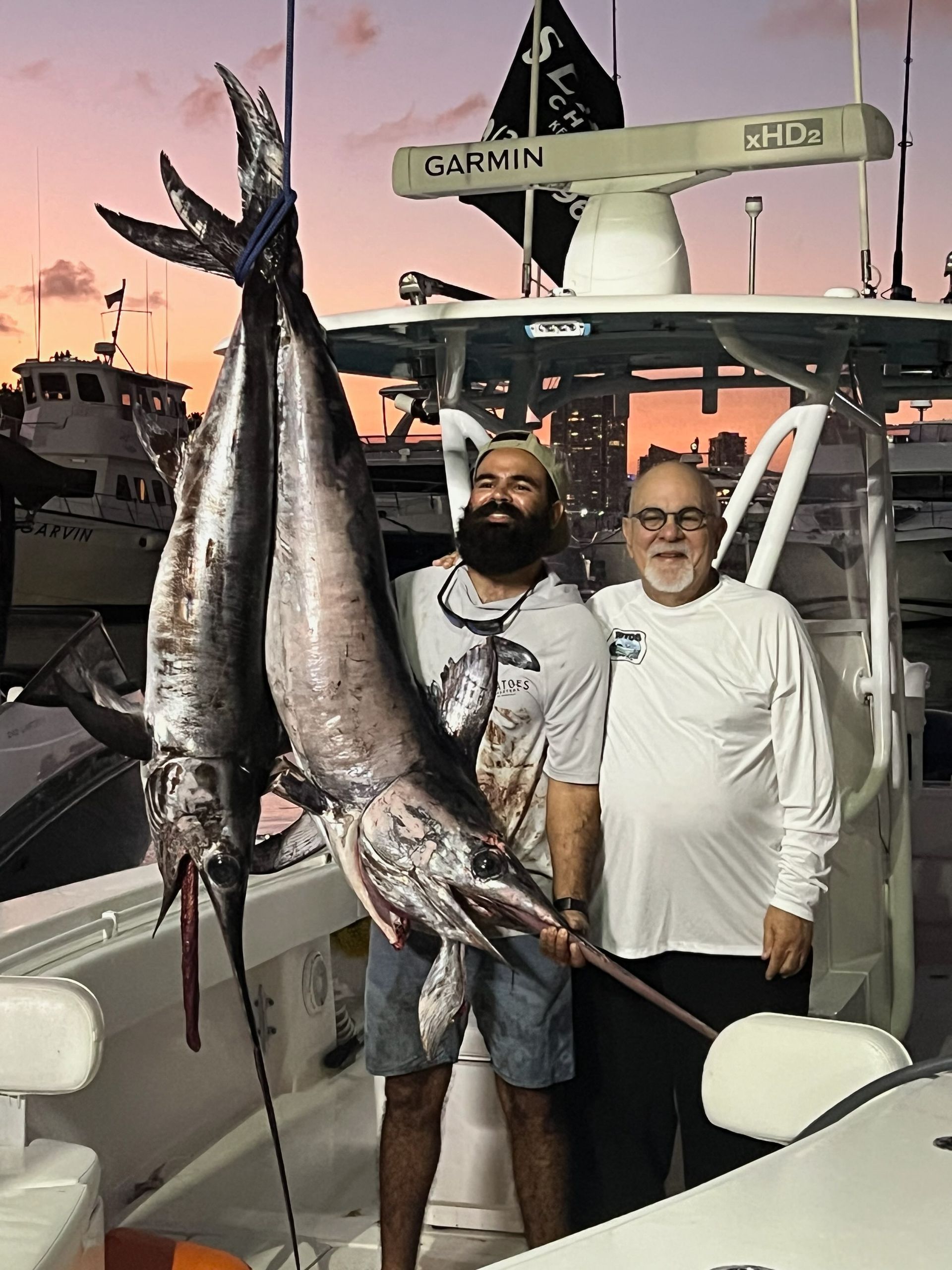 Two men are standing on a boat holding a large fish.