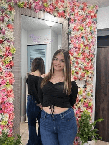 A woman is standing in front of a mirror in front of a wall of flowers.