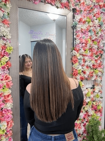 A woman is standing in front of a mirror in front of a wall of flowers.